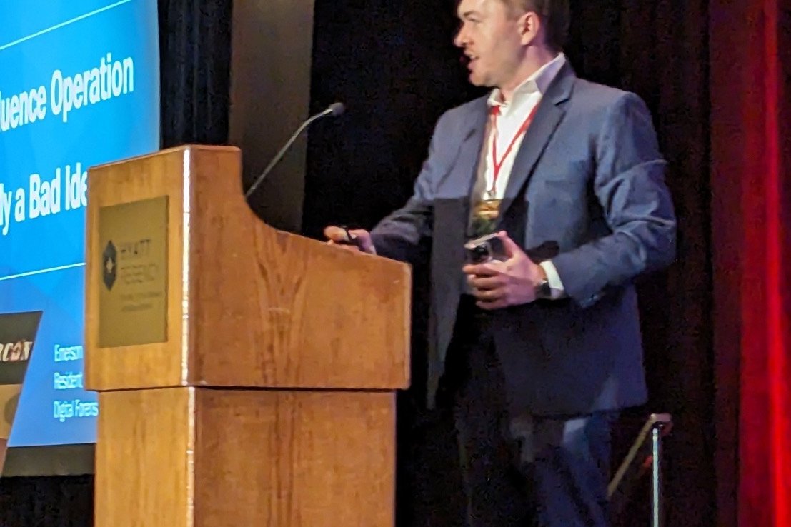 Presenting the “Why Your Influence Operation Is Probably a Bad Idea” talk at a CYBERWARCON lectern