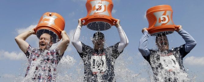 Three men dumping orange buckets of ice water over their heads outdoors as part of the Ice Bucket Challenge.