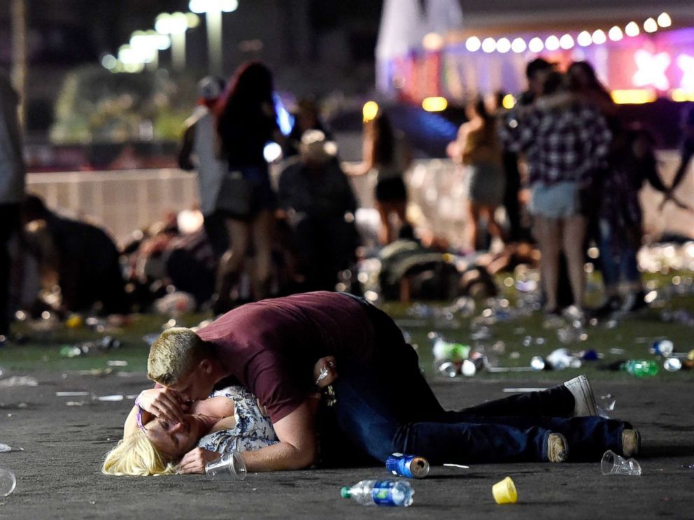 A man shields a woman lying on the ground amid scattered debris and bystanders, at the scene of the Las Vegas mass shooting.