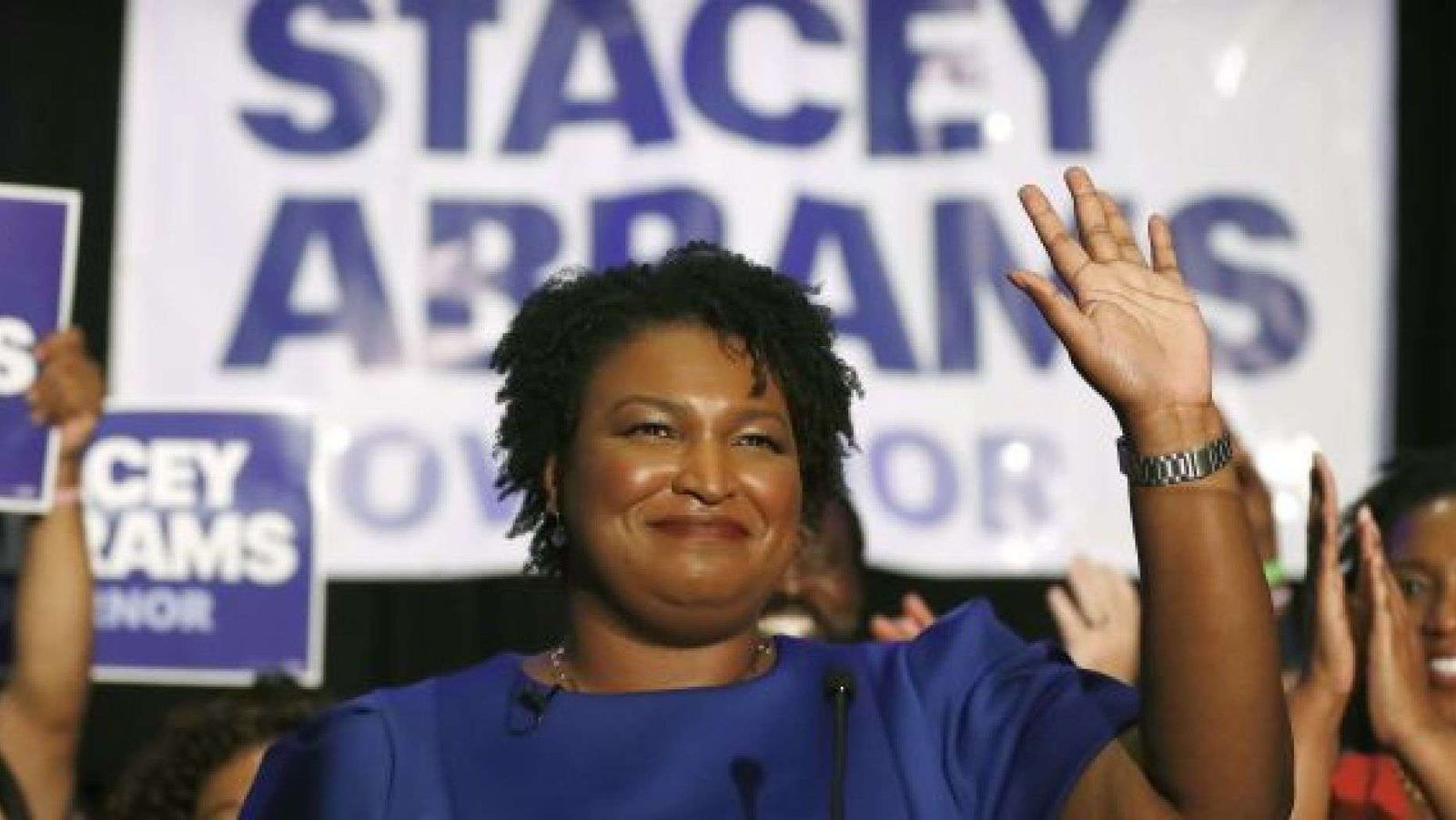 Stacey Abrams waving to a crowd in front of "Stacey Abrams for Governor" campaign signs.