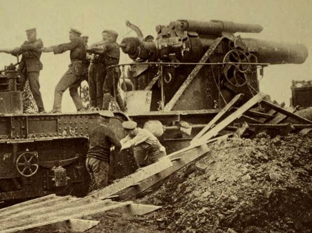 Black-and-white historical photo of soldiers loading a large WWI-era railway gun.