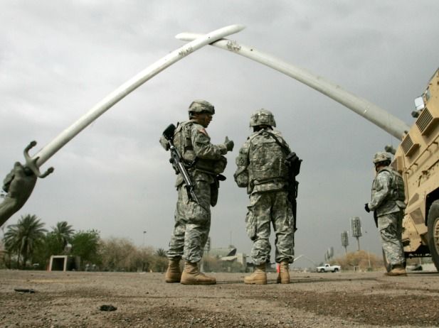 U.S. soldiers stand beneath the crossed-sabers Hands of Victory monument in Baghdad, beside an armored vehicle.